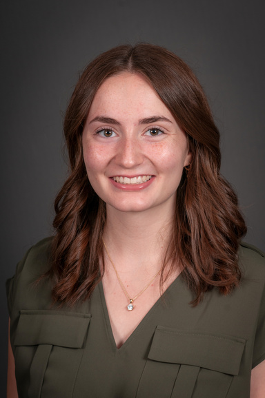 A woman in an olive green shirt smiles in front of a grey backdrop.