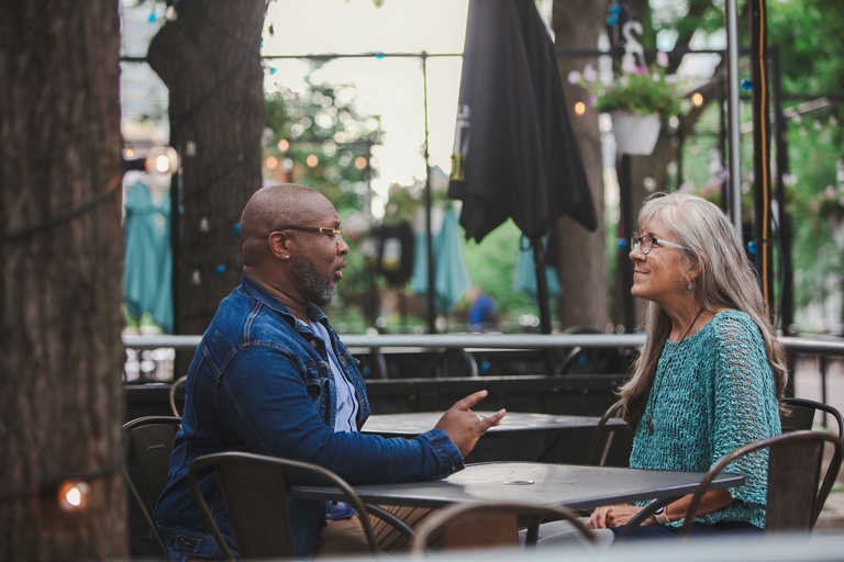 Two people sit at a table on an outdoor patio. 