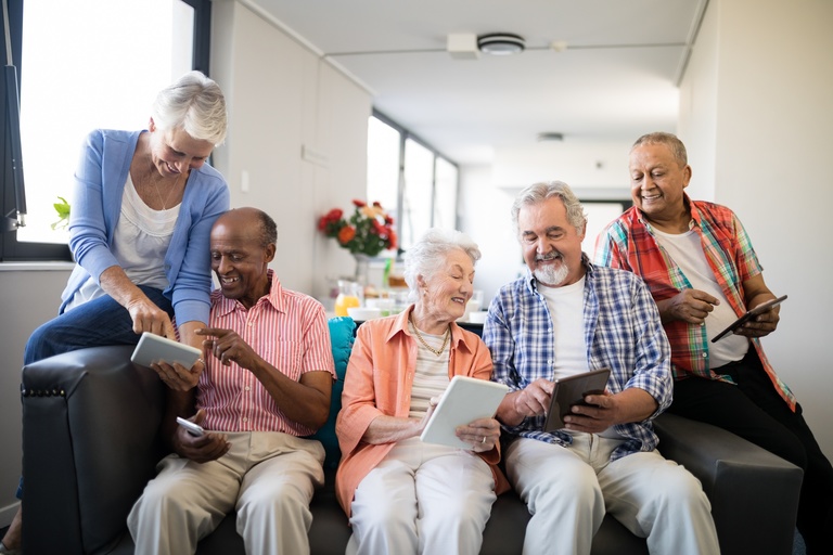5 older adults sit on a couch looking at tablets together.