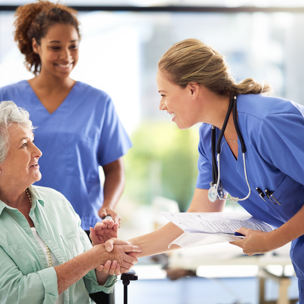 Three people are in the photo. One is sitting in a wheelchair, one is pushing it, and the third is bending down to shake the hand of the person in the wheelchair.