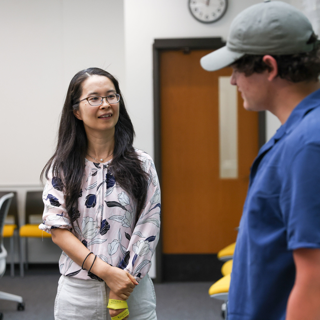 Two people stand talking in a classroom.