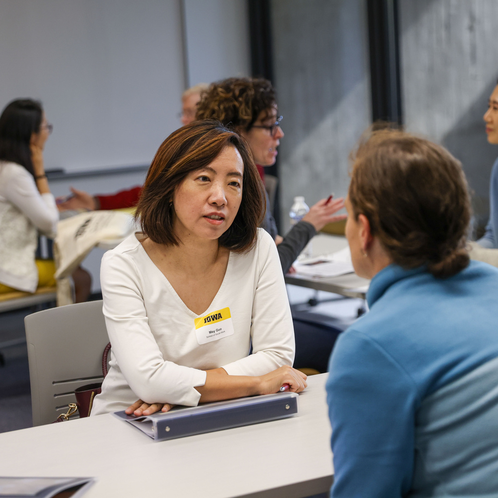 Two people sit across the table from one another, talking. Others are doing the same in the background.
