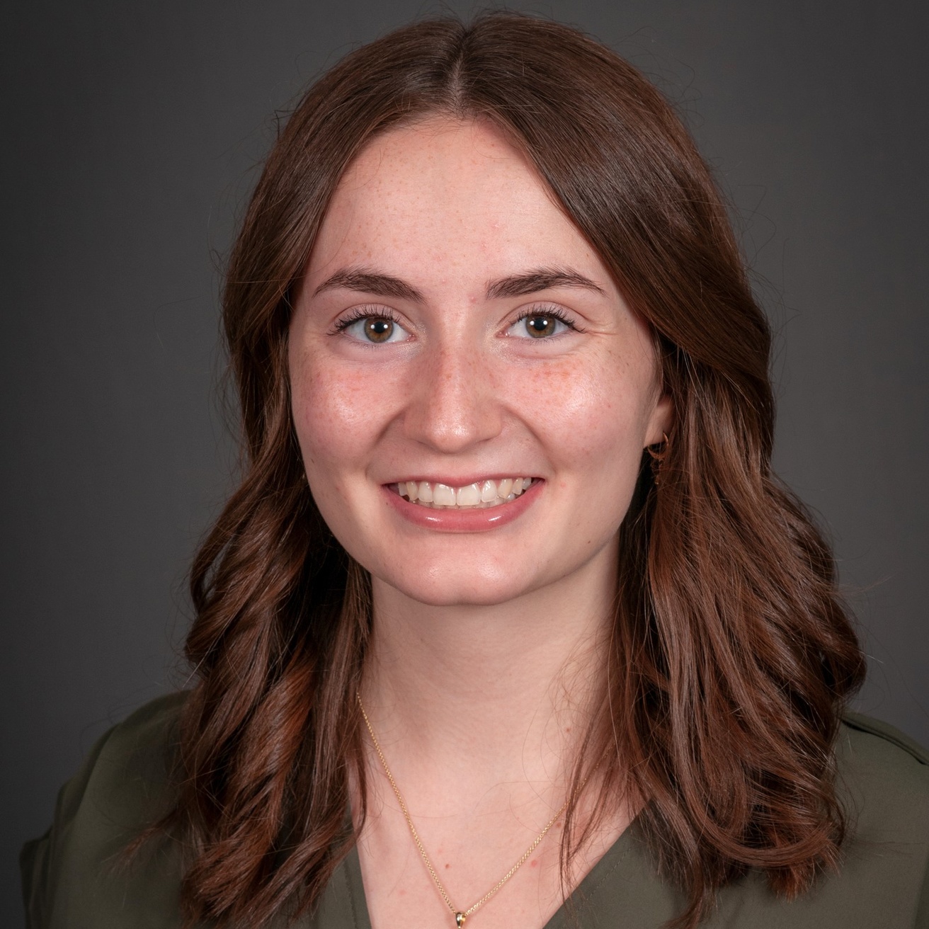 A woman in an olive green shirt smiles in front of a grey backdrop.