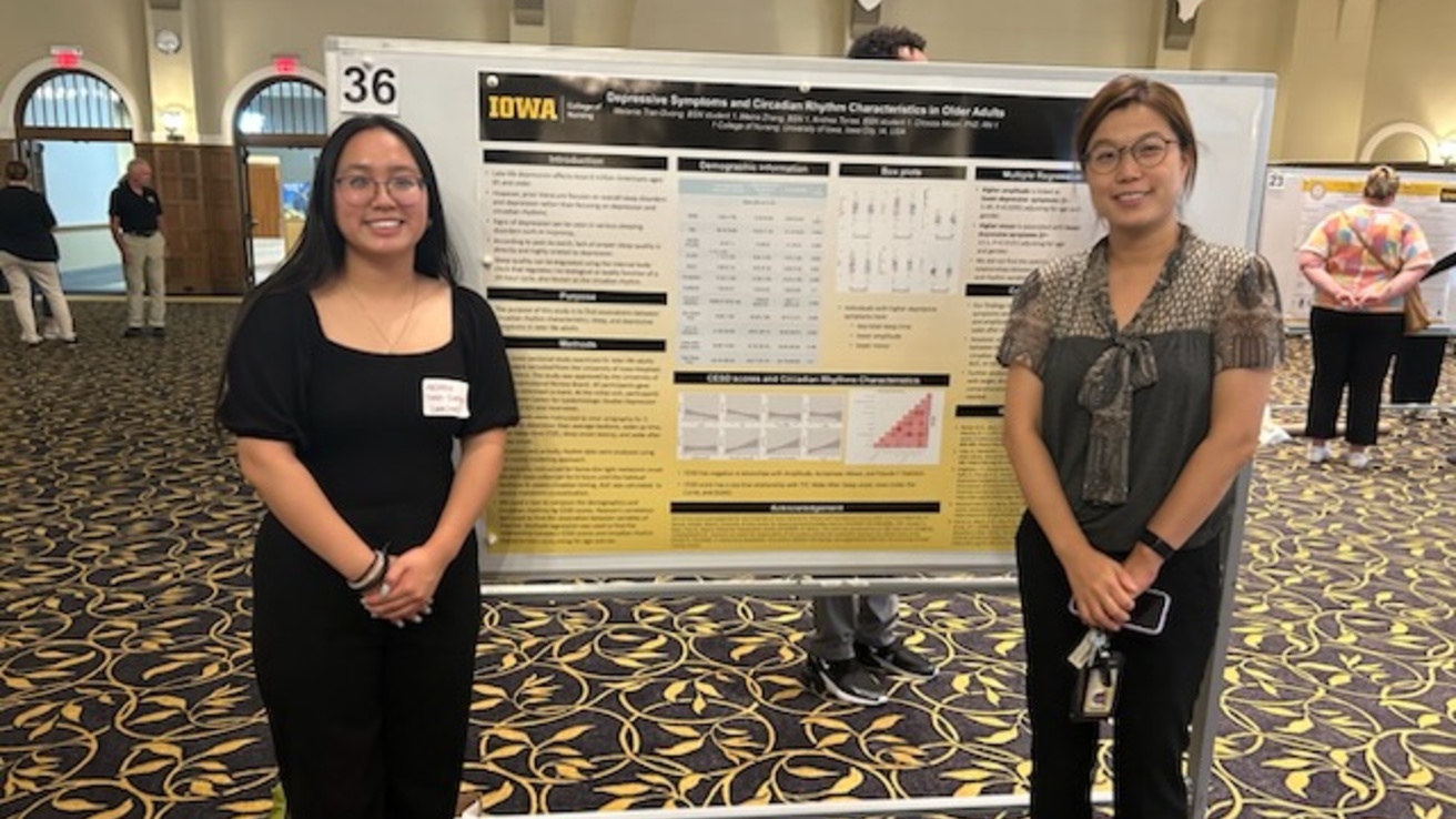 Two people stand in front of a research poster in a ballroom.