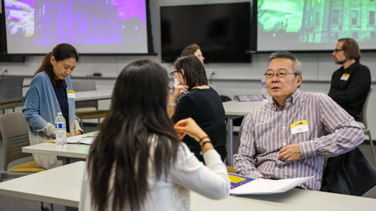 Two people sit across the table from one another, talking. Others are doing the same in the background.